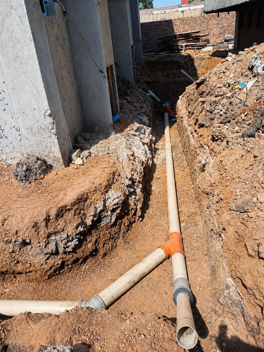 PVC soil pipes meeting at a junction fitting in an open trench beside a building